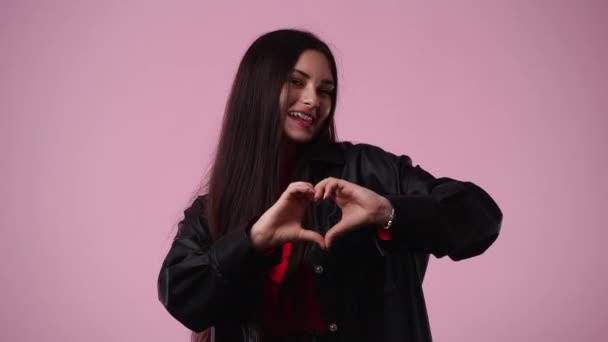 ピンクの背景に彼女の手で心の形を作る女の子の4Kビデオ 愛の感情の概念 — ストック動画