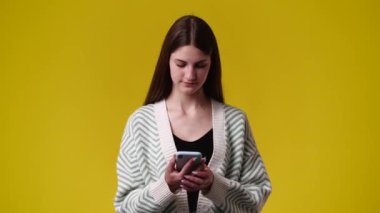 Sarı arka planda telefonunu kullanan bir kızın 4K videosu. Duyguların kavramı.