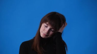Mavi arka planda poz veren bir kızın 4K videosu. Duyguların kavramı.