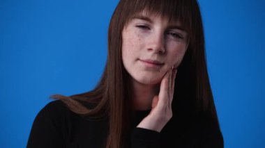 Mavi arka plan yüzünden dişi ağrıyan bir kızın 4K videosu. Duygular kavramı..