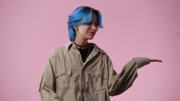 4Kビデオの1人の女の子の青い髪が右を指して ピンクの背景に親指を表示します 感情の概念 — ストック動画