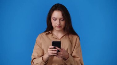 Mavi arka planda telefonla mesaj yazan bir kızın 4K videosu. Duyguların kavramı.