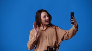 Mavi arkaplanda biriyle görüntülü konuşma yapan bir kızın 4K videosu. Duyguların kavramı.