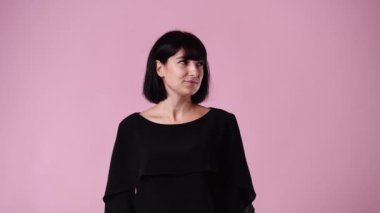 Bir kadının 4K videosu etrafa bakıyor ve pembe arka planda sessizlik işareti gösteriyor. Duyguların kavramı.