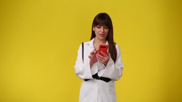 電話でテキストを入力し 黄色の背景の上に左を指している1人の女性の4Kスローモーションビデオ 感情の概念 — ストック動画