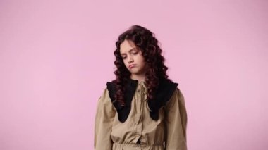 Pembe arka planda mutsuz poz veren genç bir kızın 4K videosu. Duyguların kavramı.