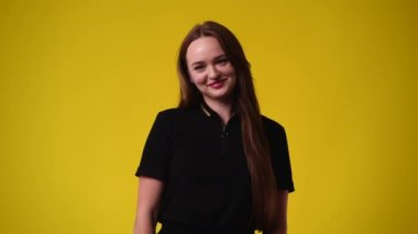 Sarı arka planda tatlı tatlı gülümseyen tatlı bir kızın 4K yavaş çekim videosu. Duyguların kavramı.