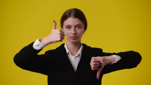片方の手で親指を上げ もう一方の手で親指を黄色い背景の上に押し下げる1人の少女の4K動画 感情の概念 — ストック動画