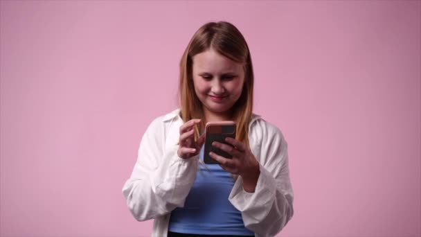 Video Una Chica Que Usa Teléfono Sonríe Sobre Fondo Rosa — Vídeos de Stock