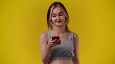 Sarı arka planda telefonunu kullanan bir kadının 4K videosu. Duygu kavramı.