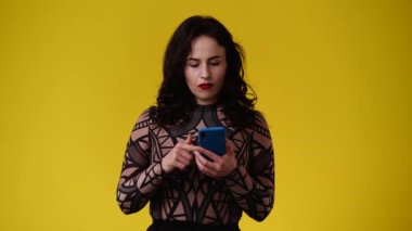 Sarı arka planda telefonunu kullanan bir kızın 4K videosu. Duyguların kavramı.