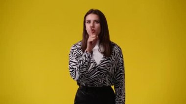 Sarı arka planda sessizlik işareti gösteren bir kızın 4K videosu. Duyguların kavramı.