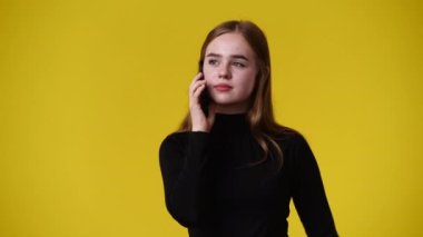 Sarı arka planda telefonu kullanan bir kızın 4K videosu. Fikirleri olan bir kız kavramı..