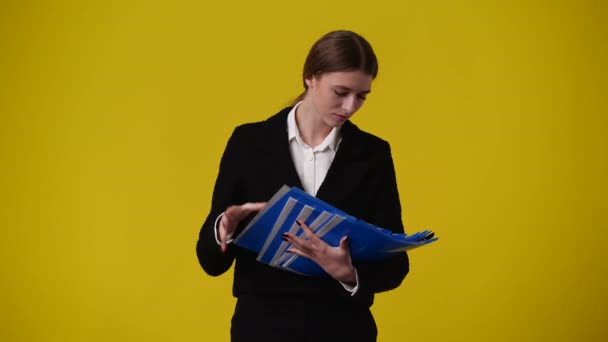 一个女孩在黄色背景的不同文件夹中寻找东西的4K视频 情绪的概念 — 图库视频影像