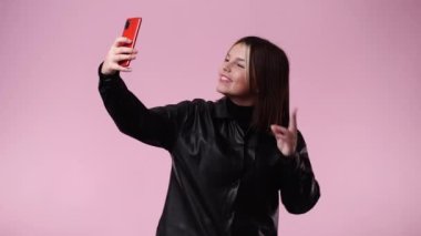 Pembe arka planda telefonundan selfie çeken bir kızın 4K videosu. Duyguların kavramı.