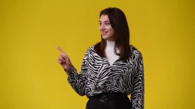 Sol tarafı işaret eden ve sarı arka planı gösteren bir kızın 4K videosu. Duygu kavramı.