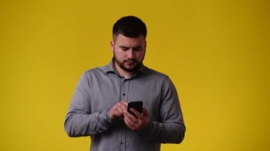 Sarı arka planda telefonu kullanan bir adamın 4K videosu. Duyguların kavramı.