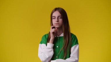 Sarı arka planda kurnaz yüz ifadesi olan bir kızın 4K videosu. Fikirleri olan kız kavramı.