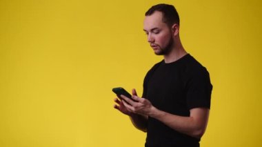 Sarı arka planda telefonu kullanan bir adamın 4K videosu. Duyguların kavramı.