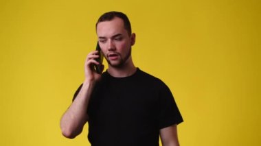 Sarı arka planda telefonda birine öfkeyle bağıran bir adamın 4K videosu. Duyguların kavramı.
