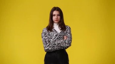 4k video of one girl who crosses her arms and responds negatively to something over yellow background. Concept of emotions.