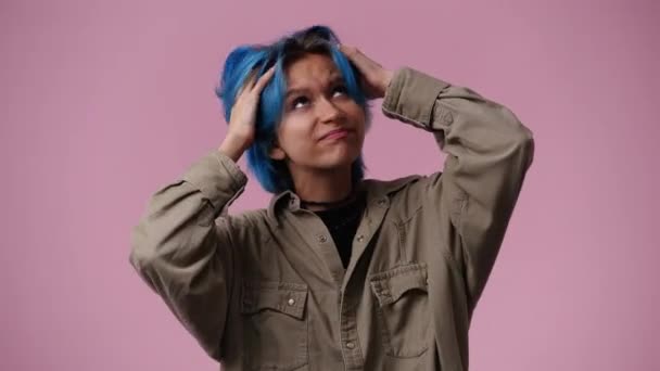 ピンクの背景で頭を掻いているある女の子の4Kビデオ 感情の概念 — ストック動画