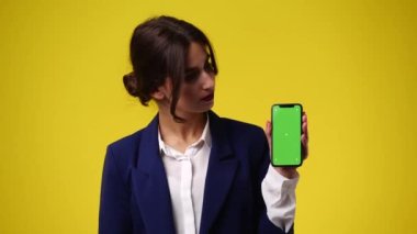 Telefonda bir şey gösteren ve sarı arka planda bundan hoşlanmayan bir kızın 4K videosu. Duyguların kavramı.