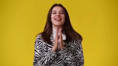 4k video of one girl claps his hands and smiling over yellow background. Concept of emotions.