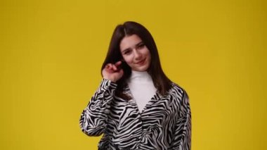 Saçlarını tatlı tatlı kıvıran ve sarı arka planda bir şey düşünen bir kızın 4K videosu. Duyguların kavramı.