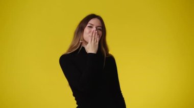 Sarı arka plan üzerinden hava öpücüğü gönderen bir kızın 4K videosu. Duyguların kavramı.