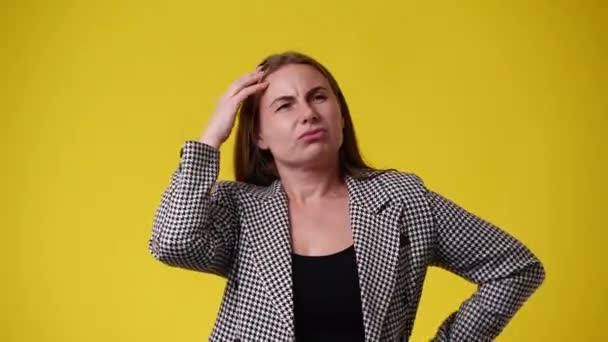 頭を掻いて黄色い背景の上に何かを考えている1人の女性の4Kビデオ 感情の概念 — ストック動画