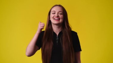 4k slow motion video of one girl showing thumbs up and smiling over yellow background. Concept of emotions.