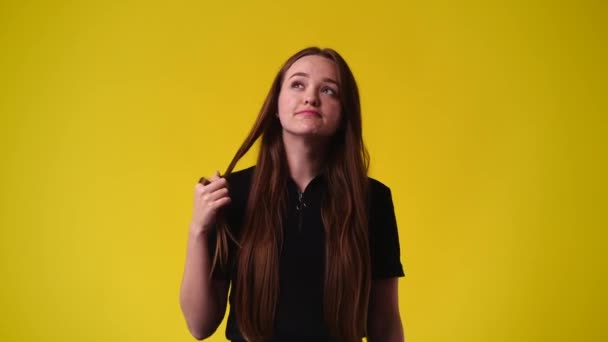 髪をカールし 黄色の背景の上に何かを考えている1人の女の子の4Kスローモーションビデオ 感情の概念 — ストック動画