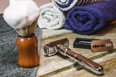 Islak tıraş malzemelerinin yatay yakın plan fotoğrafı. Parlak güvenlik jileti, köpüklü tıraş fırçası, çift taraflı jilet ve berber havluları..