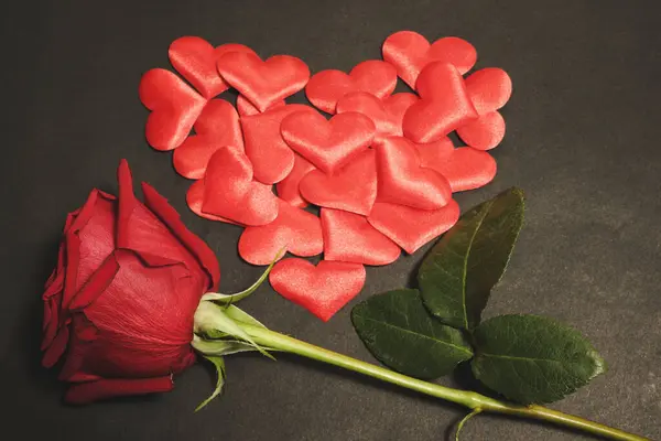 stock image Horizontal photo of voluptuous red rose and small cloth hearts, arranged in a heart shape, against dark black background. Valentines concept