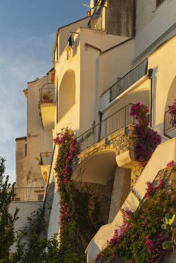 Sahildeki bir köyde, denize doğru uzanan taş basamaklı bir ara sokak. Her iki taraftaki binalar bitkilerle süslenmiş.