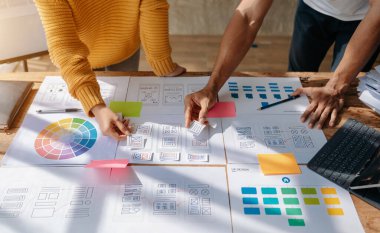 Web için UX grafik tasarımcısı uygulama geliştirme prototipi. İnsanlar ellerinde kağıtlarla masada beyin fırtınası yapıyor. 