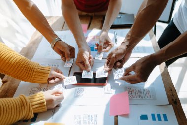 Web için UX grafik tasarımcısı uygulama geliştirme prototipi. İnsanlar ellerinde kağıtlarla masada beyin fırtınası yapıyor. 