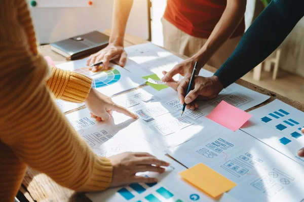 Web için UX grafik tasarımcısı uygulama geliştirme prototipi. İnsanlar ellerinde kağıtlarla masada beyin fırtınası yapıyor. 