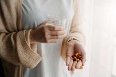 Elinde bir bardak su ve ilaç olan kadın doktorunun yazdığı ilaçları alacak. 