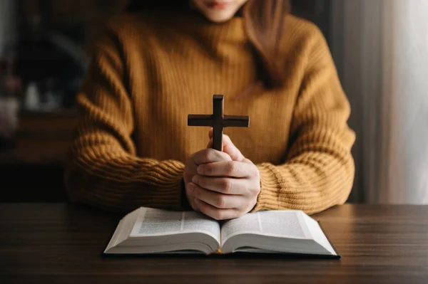 cropped view of religious woman praying, Hands at table with cross and bible book