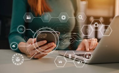 Ofis masasında dizüstü bilgisayarla otururken elinde cep telefonu olan bir iş kadını görüntüsü. dijital sanal simgeler 