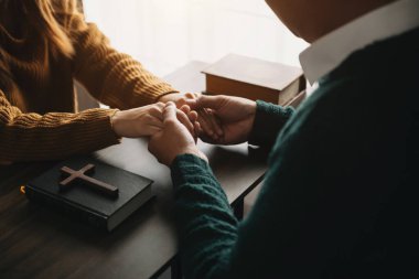 Erkek ve kadın el ele tutuşuyor. Masanın üzerinde haç ve İncil kitabı 