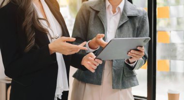 İki iş adamı akıllı telefondan konuşuyor ve ofiste dizüstü bilgisayar kullanıyorlar.