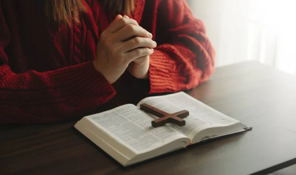 cropped view of religious woman praying, Hands at table with cross and bible book
