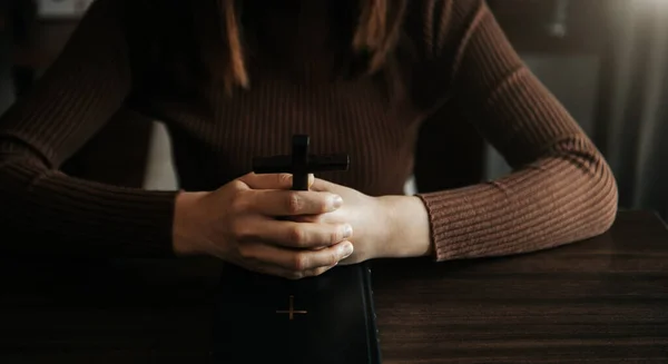 cropped view of religious woman praying, Hands at table with cross and bible book