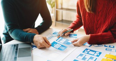 Web projesi için UX tasarım uygulama geliştirme prototipi. İnsanlar ellerinde kağıtlarla masada beyin fırtınası yapıyor. 