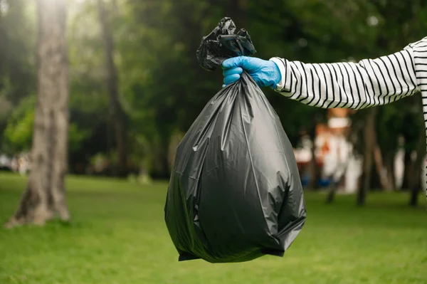 stock image Hand holding garbage black bag putting in to trash to clean. Clearing, pollution, ecology and plastic concept