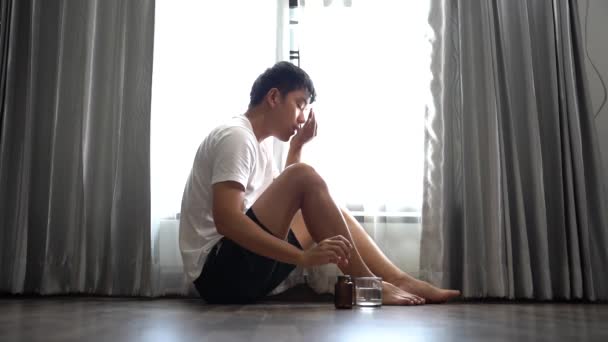 悲しい男が窓の近くの自宅で床に座っていると水のガラスで丸薬を飲んで — ストック動画
