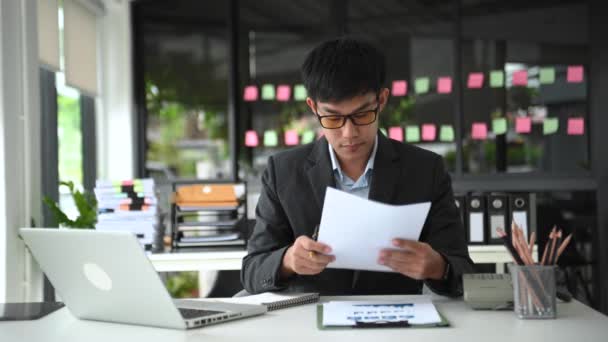 Asiático Homem Sentado Mesa Trabalho Escritório Moderno Verificando Papéis Laptop — Vídeo de Stock